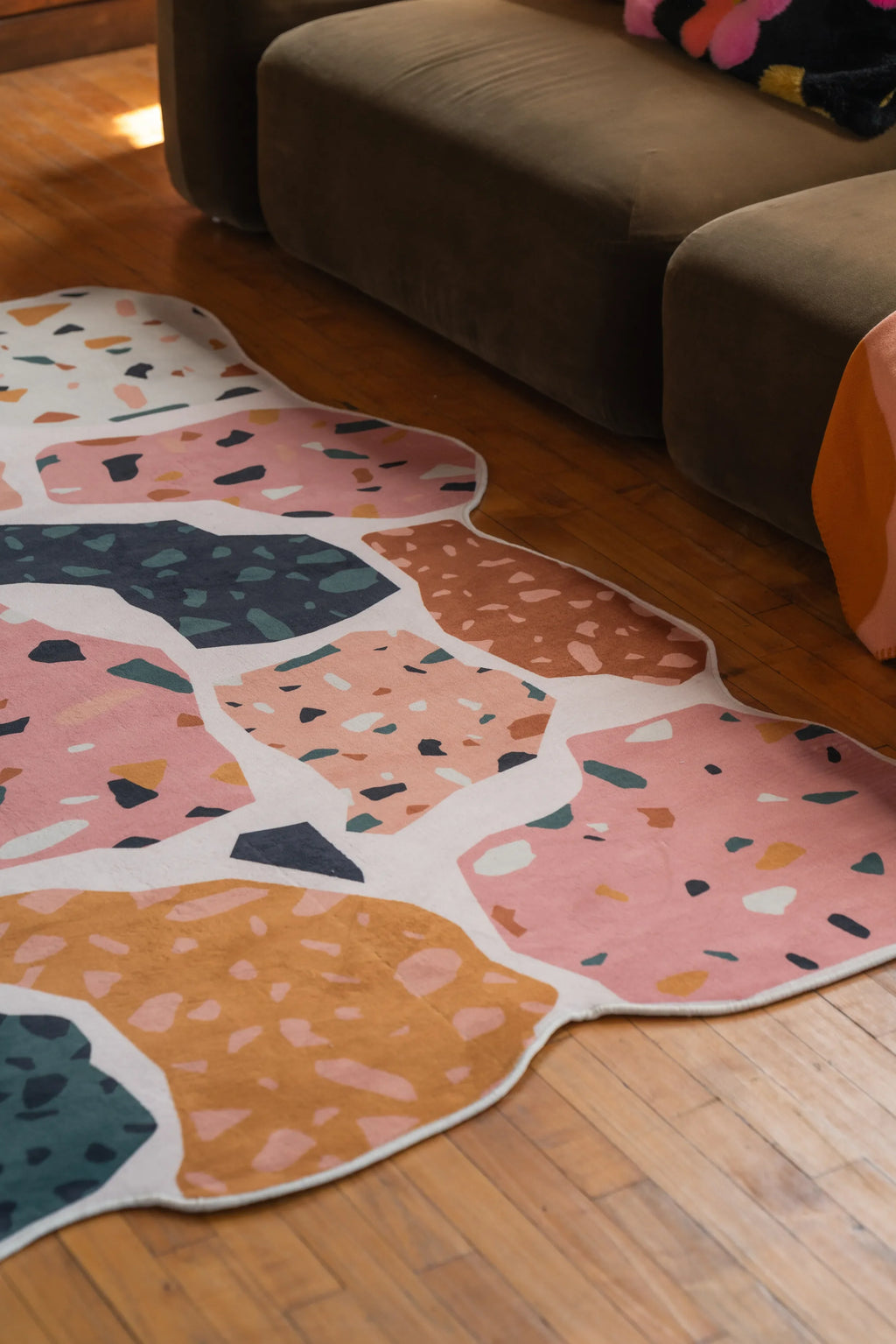 Close-up of an abstract rug with colorful terrazzo patterns in a living room, placed beside a dark brown sofa