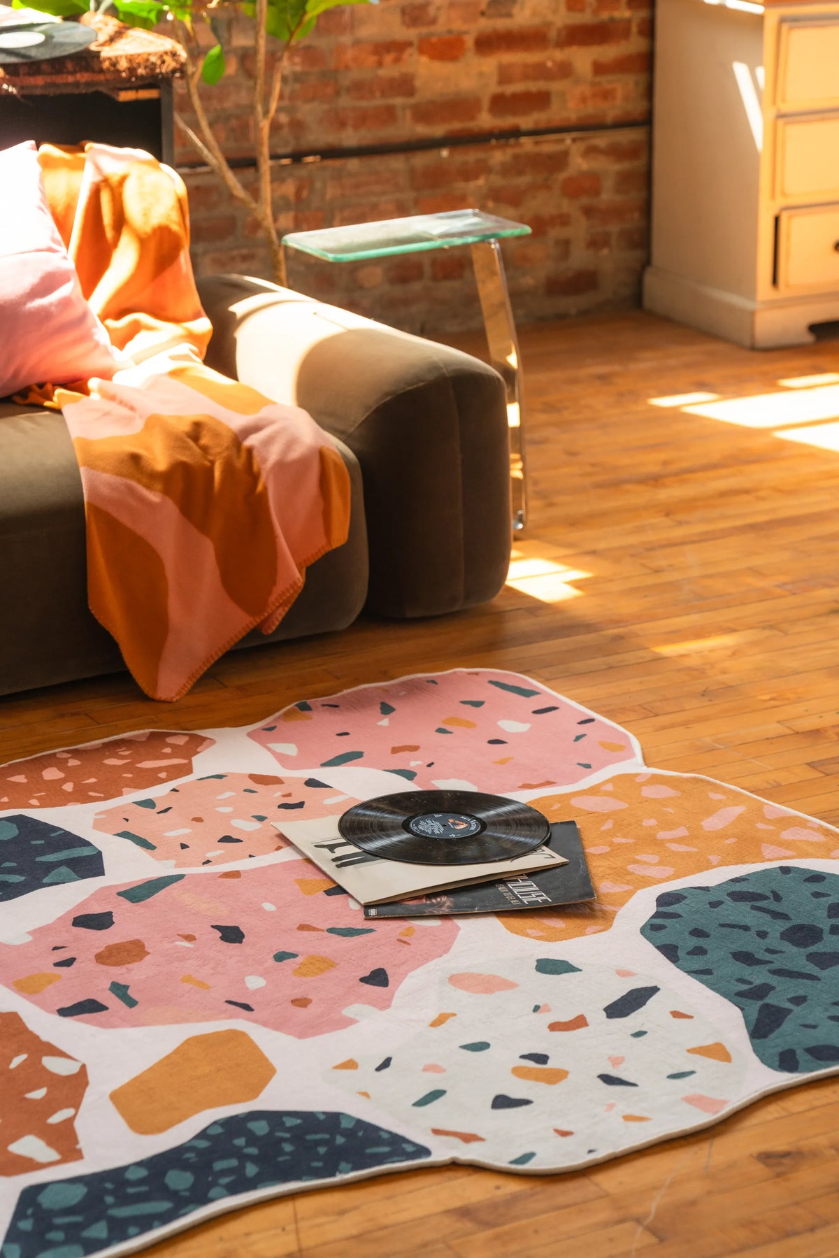 Colorful terrazzo-style abstract rug with a vinyl record and magazine on top, beside a brown sofa in a sunlit room