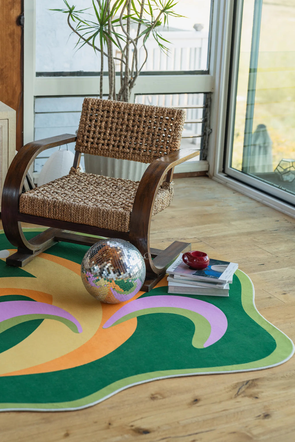 Funky bananas rug under disco ball, books, and armchair in a bright corner with wood floor and sunlight streaming in.