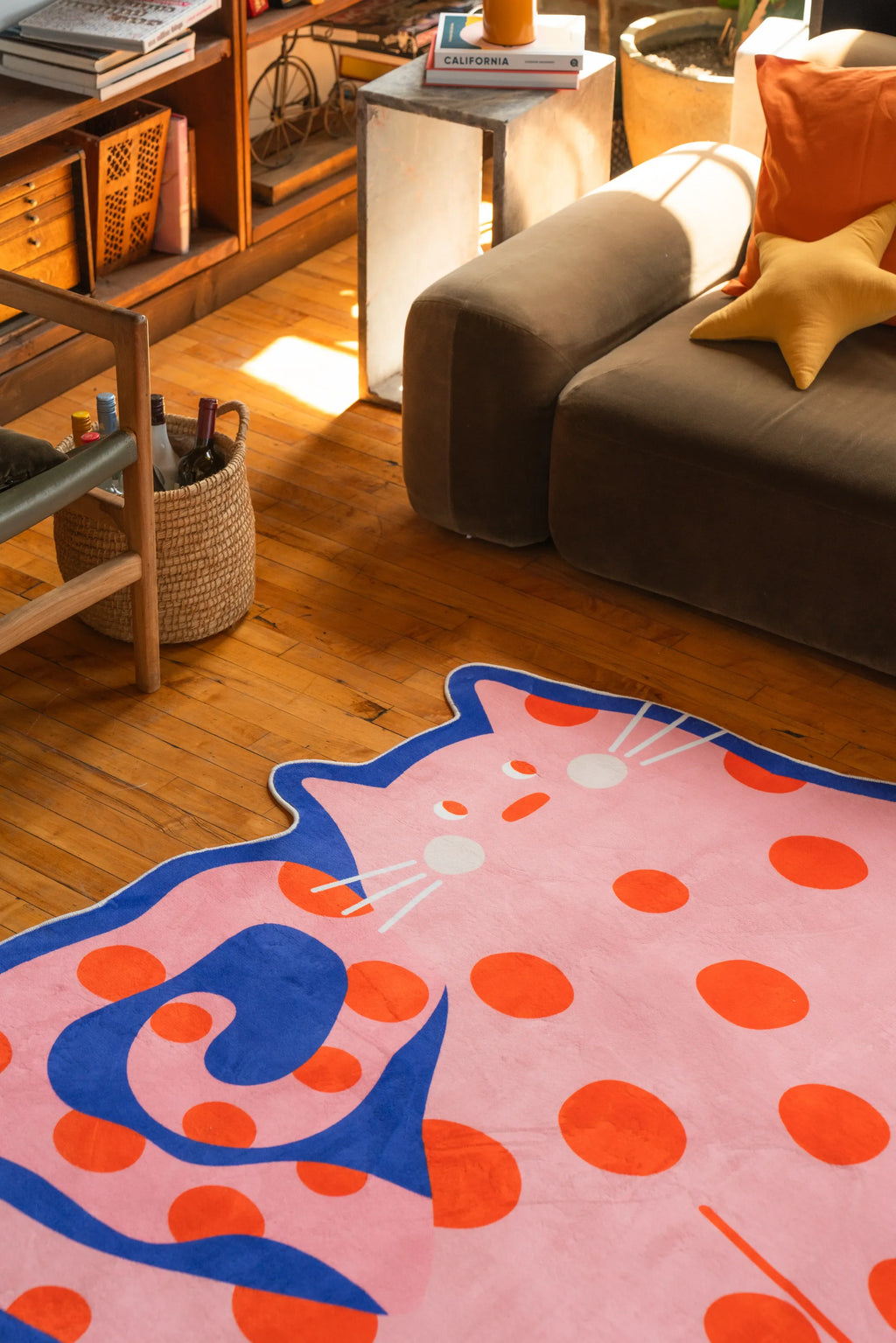 Navy blue cat-shaped rug with orange polka dots tucked beside a sofa in a softly lit space