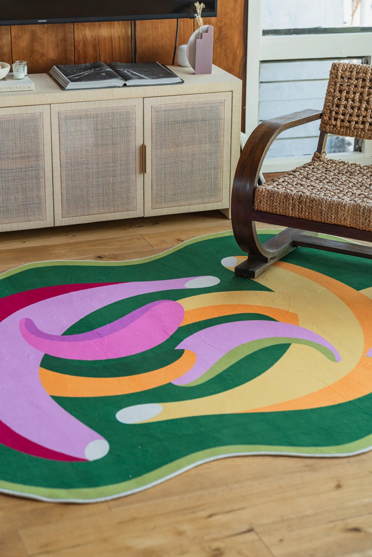 Curved chair and media console next to the playful banana rug with bold, abstract shapes in green, purple, and yellow tones.