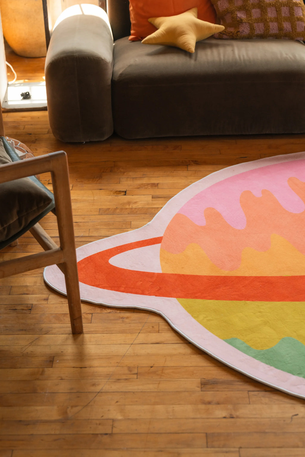 Detail of the Melting Planet Rug with sunset tones on hardwood floor beside sofa