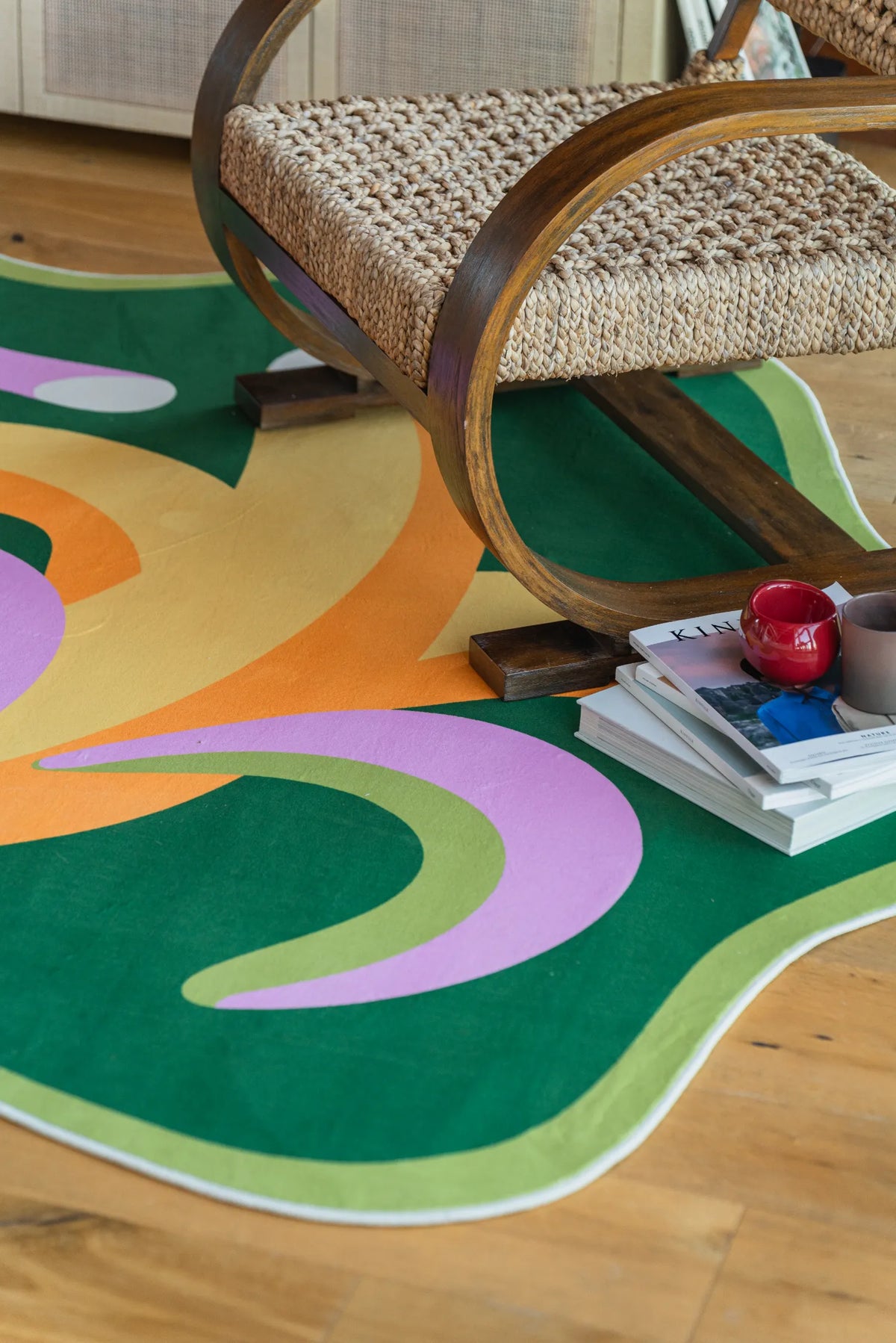 Close-up of the funky bananas rug beside a woven armchair, with books and cups arranged on the floor.