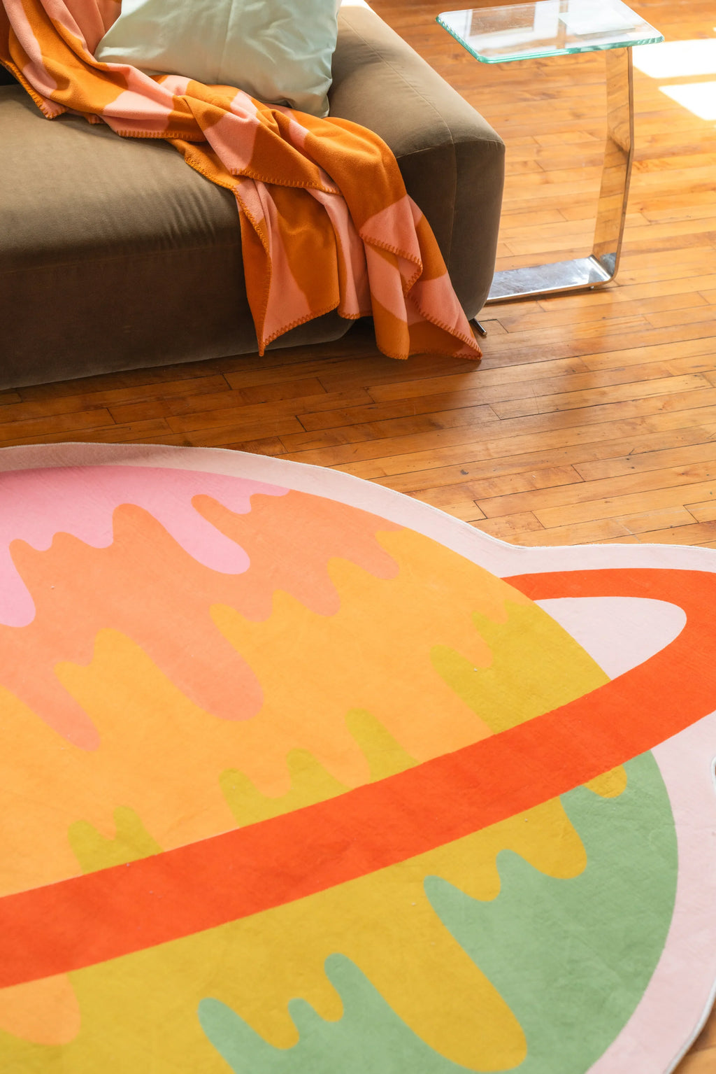 Vibrant planet area rug with orange and pink tones beside brown sofa and glass side table