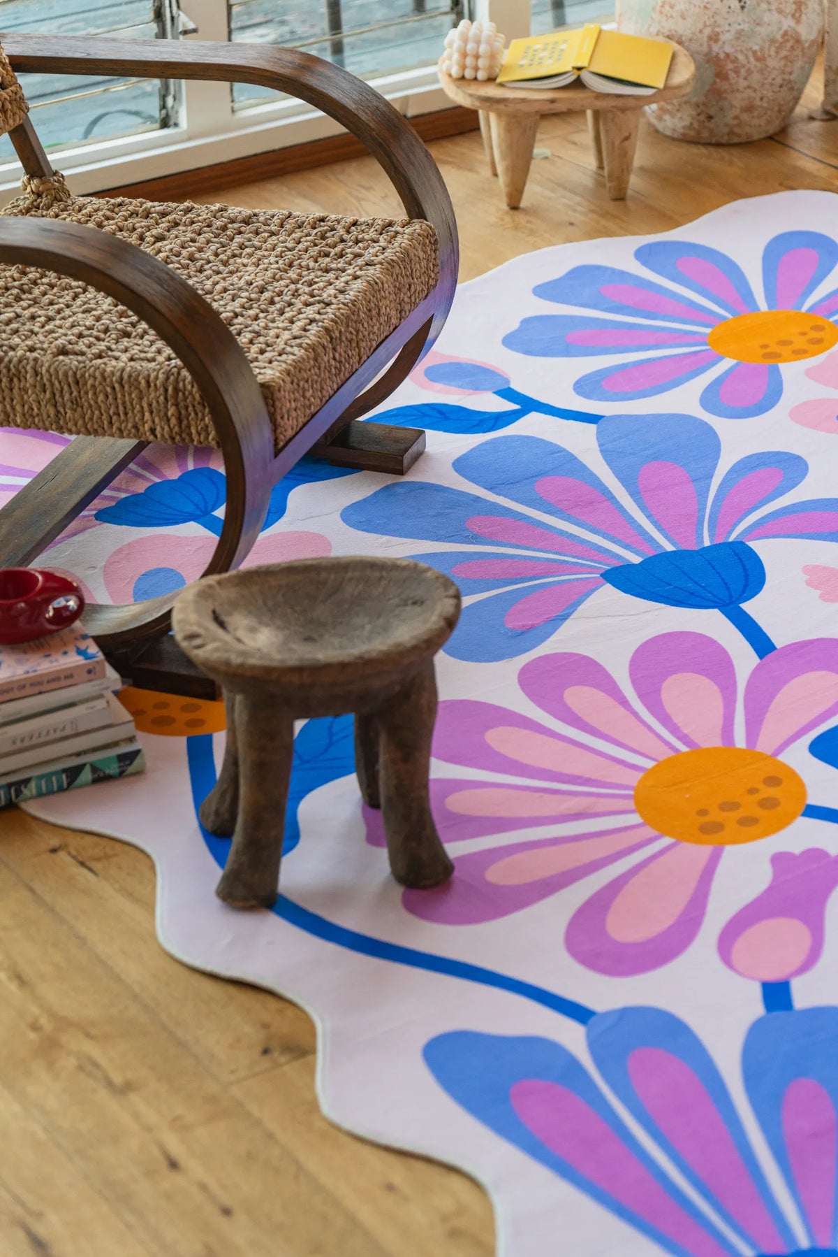Purple floral wavy rug with scalloped edge tucked beneath a curved rattan chair on wood floor.