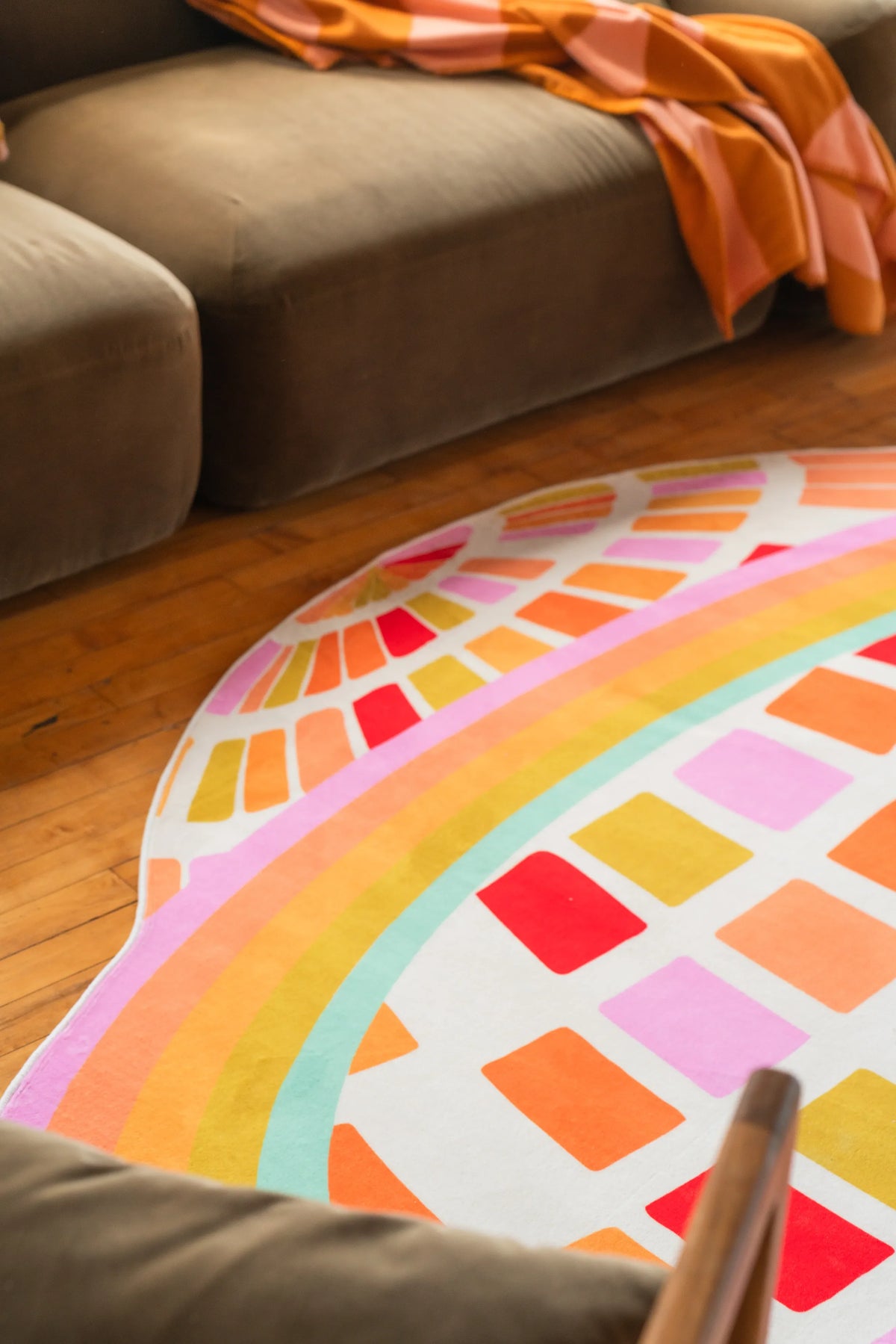 Part of the orange disco checkered rug curving near a low couch on sunlit wood floor