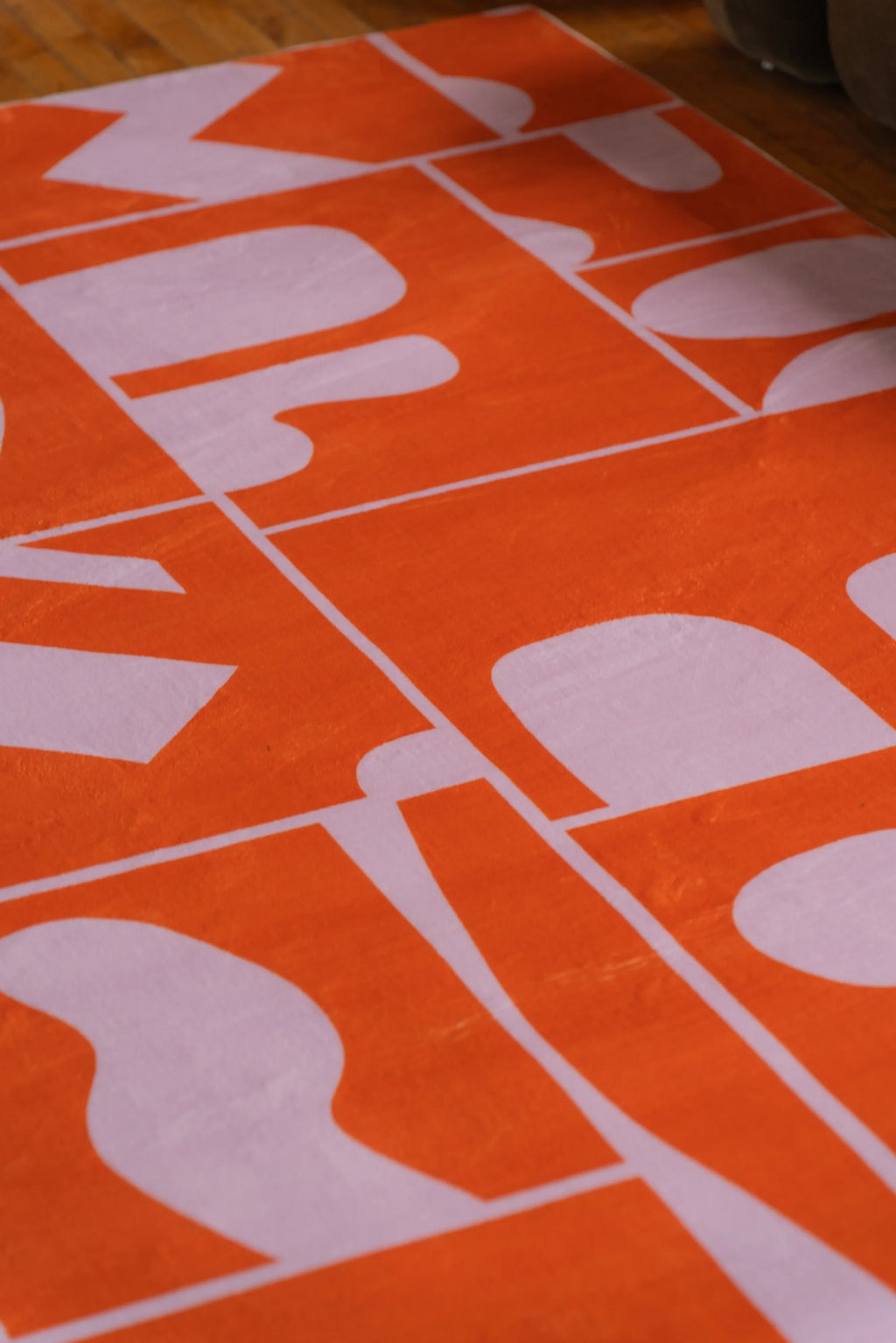 Close-up view of the Orange Geometric Patchwork Rug by Becca Franks, showcasing its playful pattern on warm-toned wood flooring