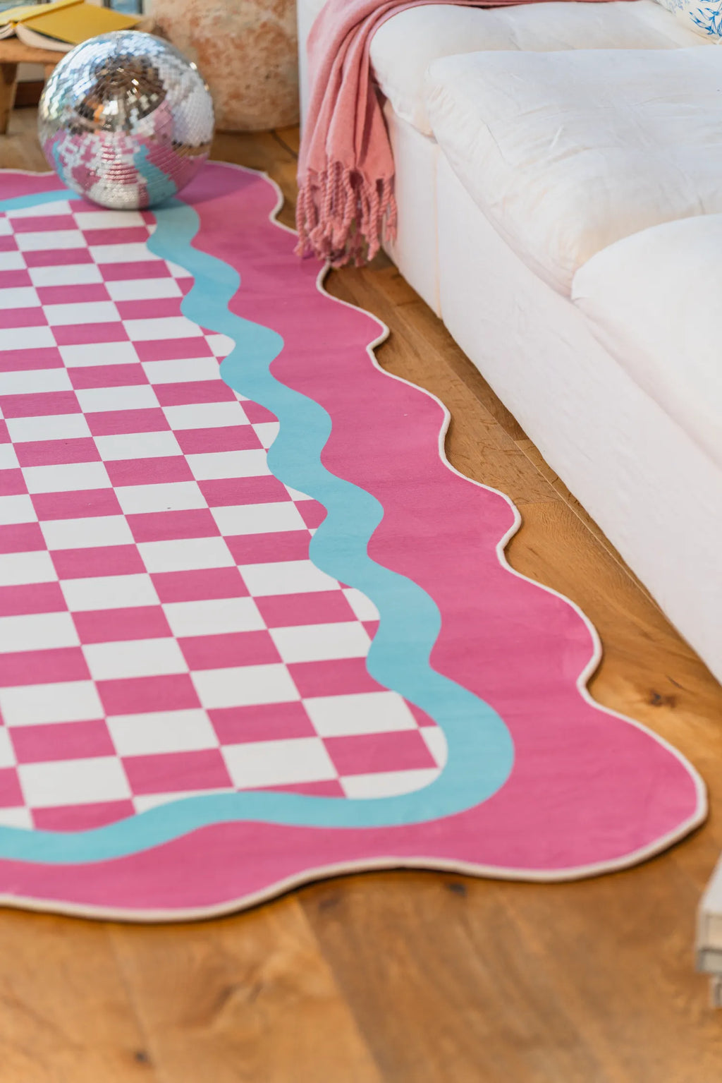 A close-up of the pink and blue lace checkered rug next to a white sofa and disco ball.