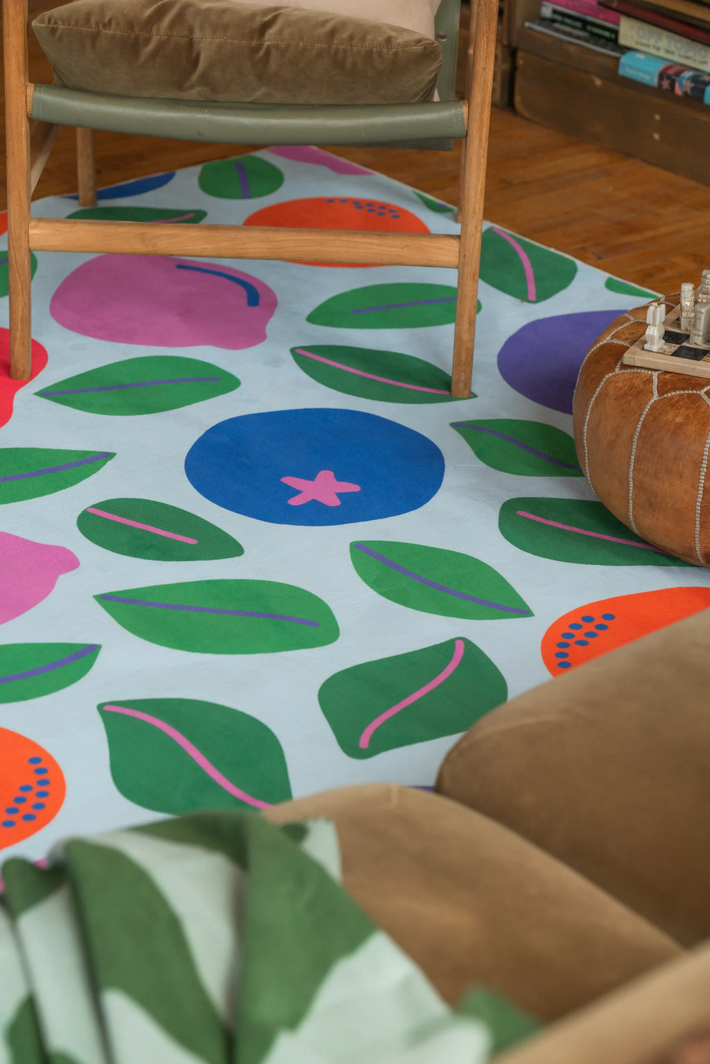 A playful rug with colorful fruit shapes extends beneath armchairs and pouf on wood floor