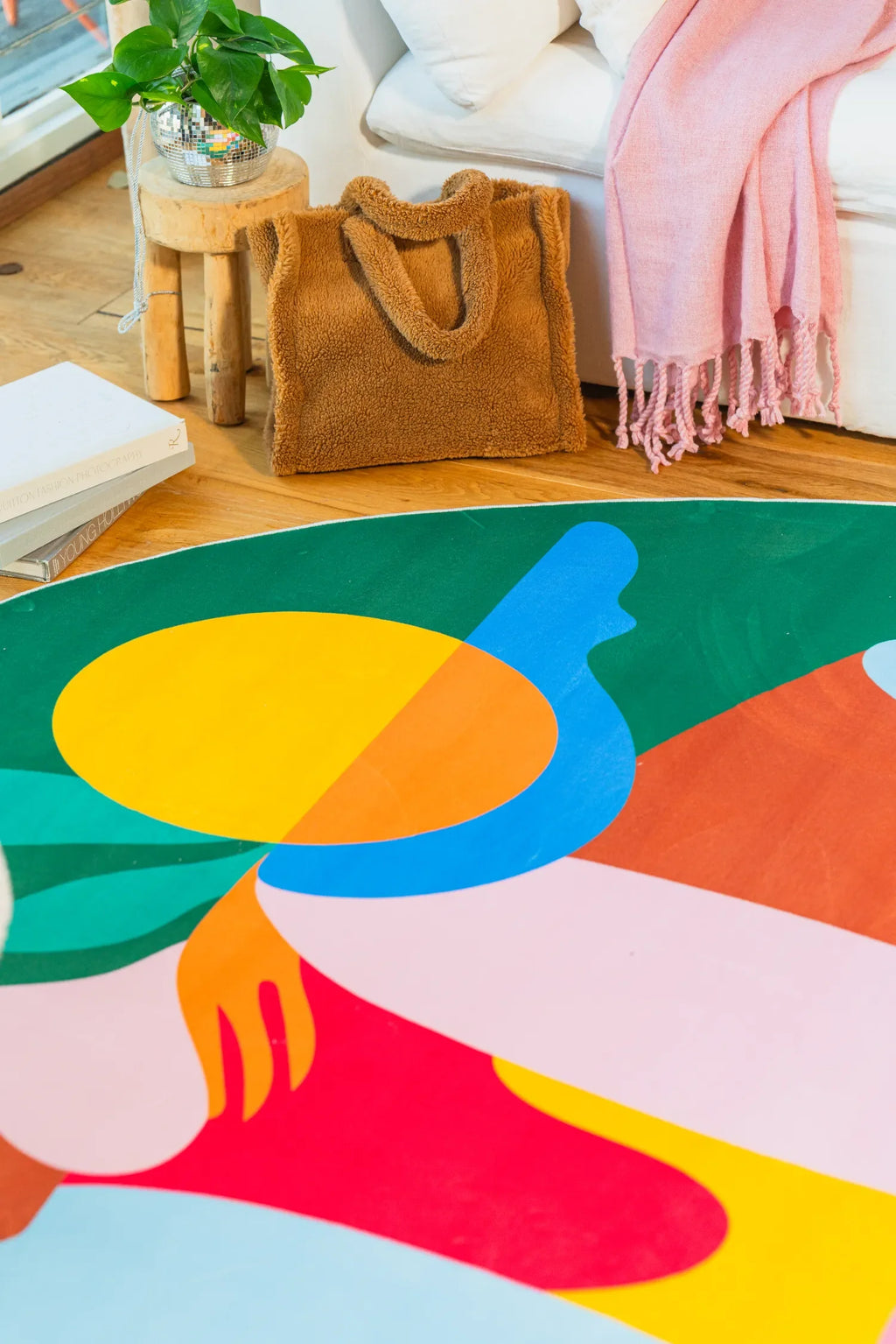 Detail of fruitvine green rug with yellow sun and red hand motif beside a white sofa and pink scarf.
