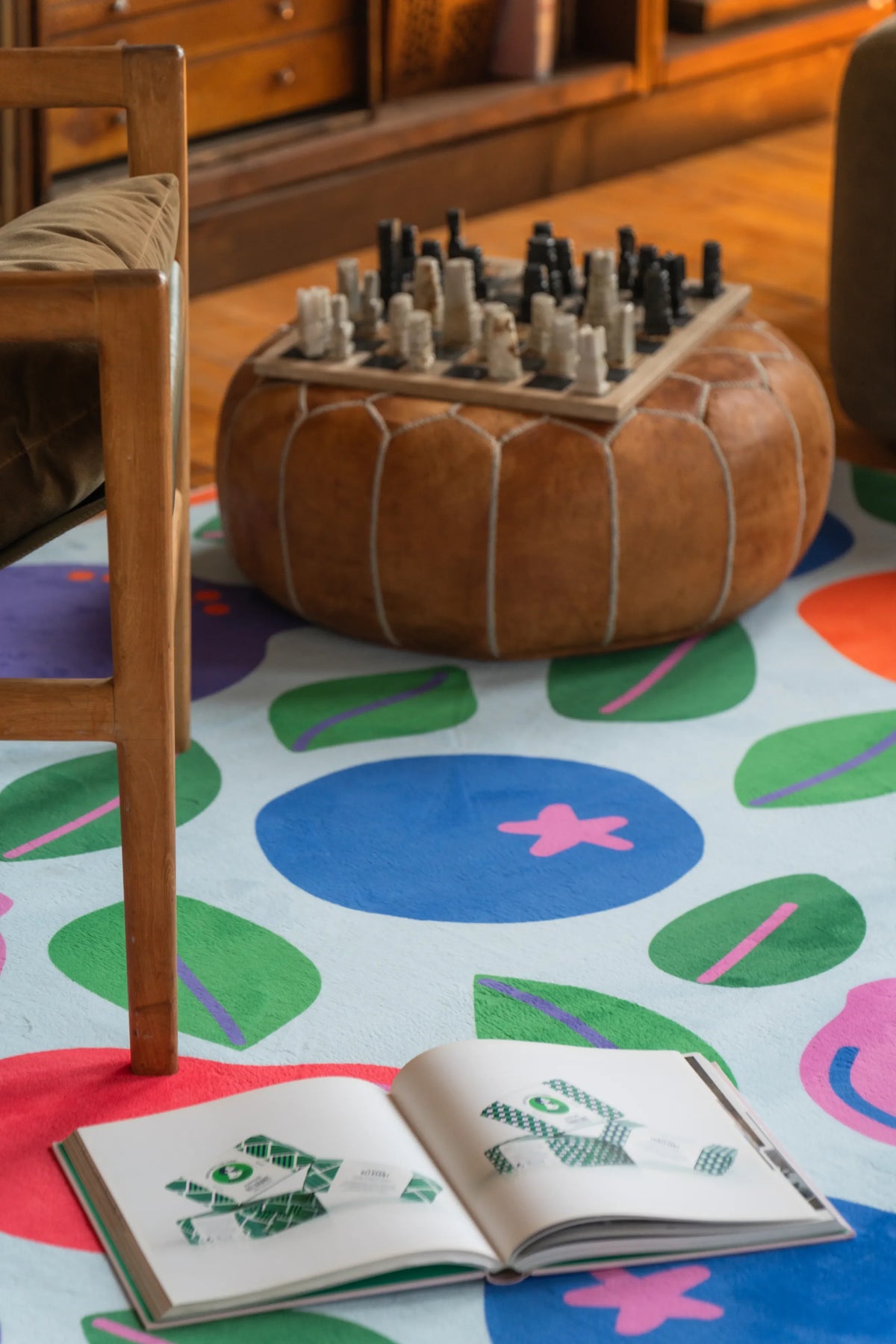 Funky rug with fruit motifs tucked between chairs and soft seating in a warm, book-lined nook