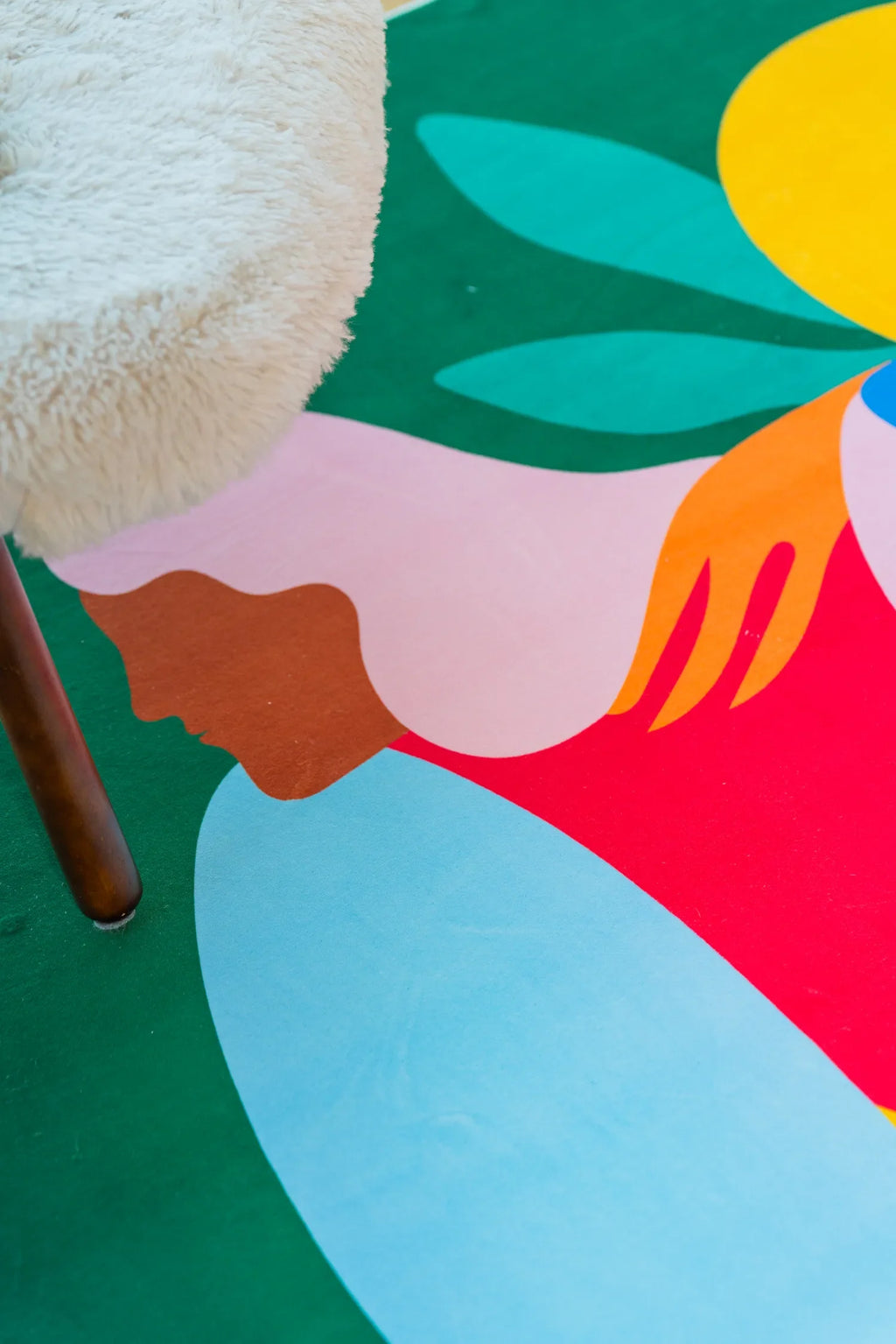 Colorful section of fruitvine green rug with abstract hand and leaf shapes beside a yellow cushion and open book.