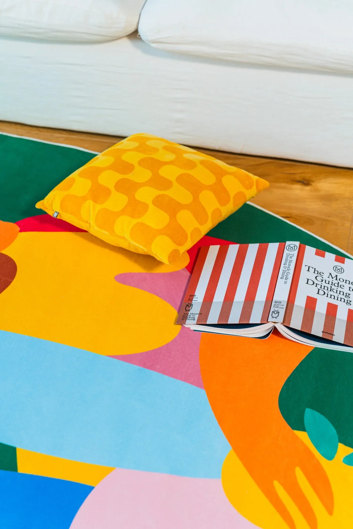 Fruitvine green rug with abstract hand and sun shapes next to a white sofa and yellow patterned cushion.