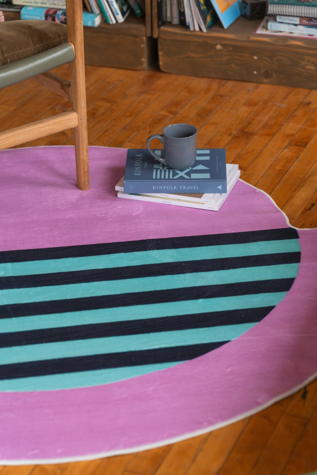 Home interior shot featuring a pastel pink circle rug with teal stripes and books stacked neatly beside a ceramic mug