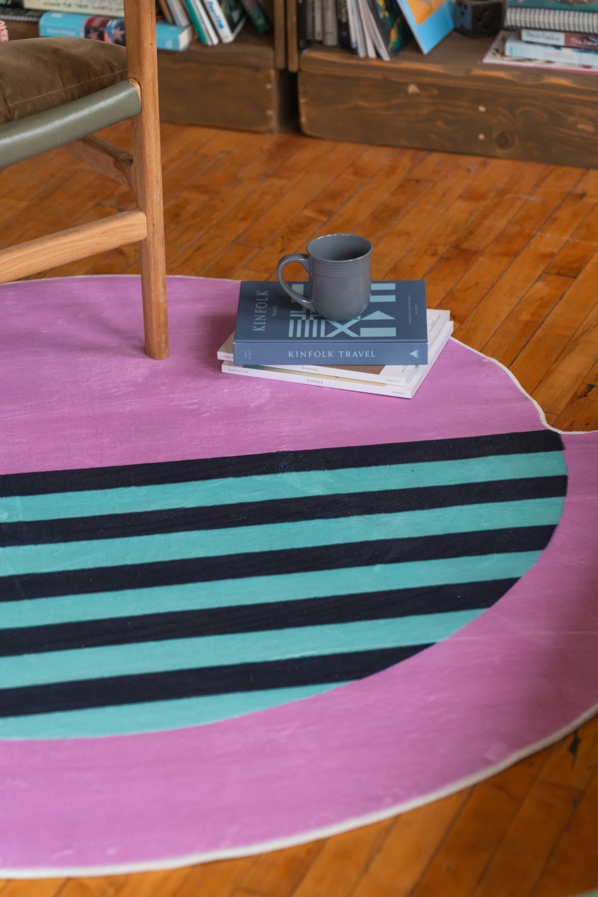 Home interior shot featuring a pastel pink circle rug with teal stripes and books stacked neatly beside a ceramic mug