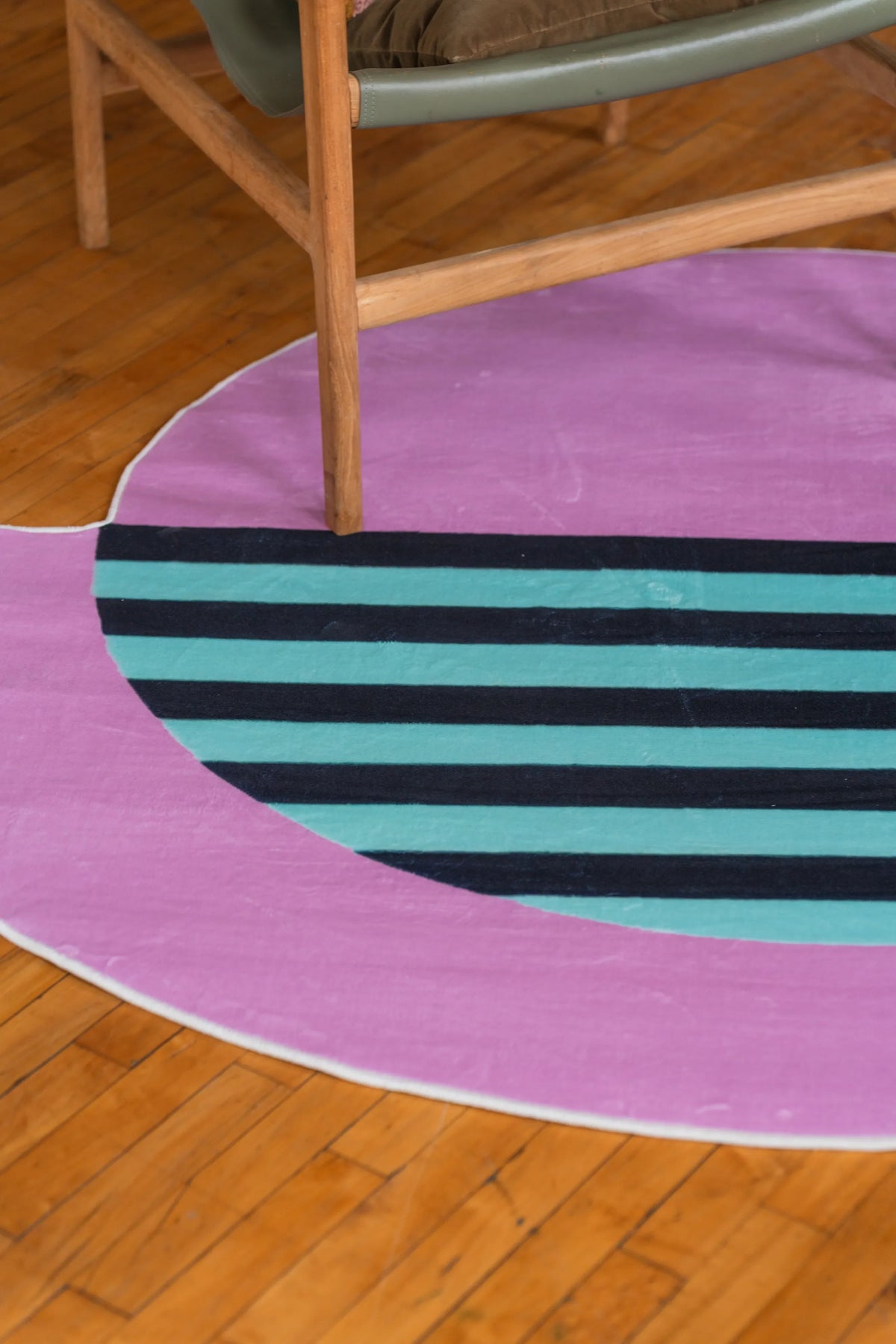 Minimalist striped pink rug with teal and black accents partially tucked beneath a mid-century chair on hardwood floors