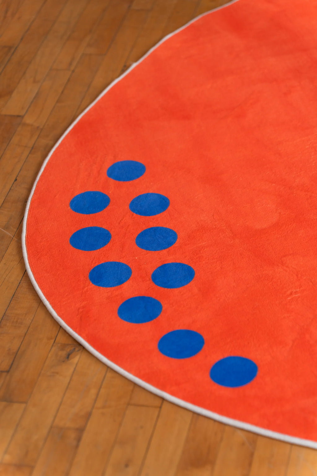 Close-up of blue dot pattern on edge of round orange minimalist rug lying on hardwood floor