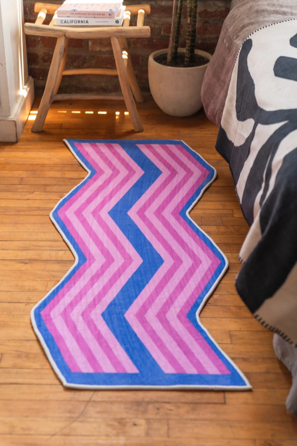 Bright pink and blue zigzag bedroom rug placed along bedside in cozy wood-floored room