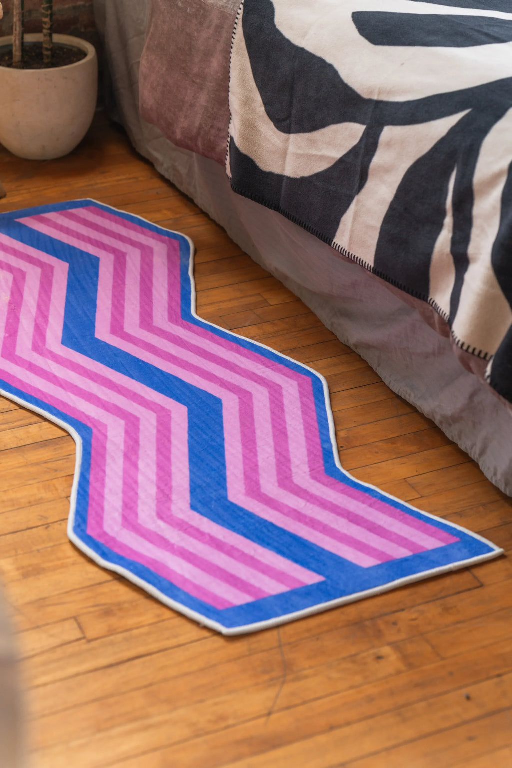 Pink Blue Zigzag Wave Rug beside bed with zebra print sheet on hardwood bedroom floor