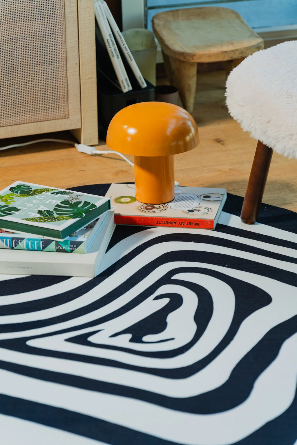 Close-up of abstract rug with orange mushroom lamp and stacked books.