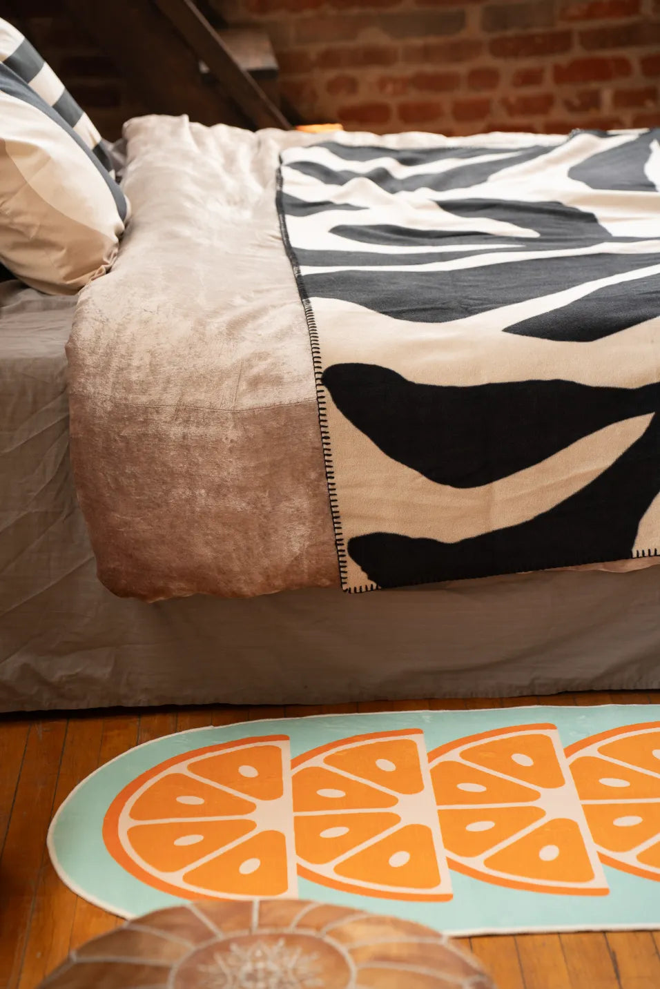 Closeup of blue fruit rug with orange wedges beside bed with neutral bedding and black and white throw, home design