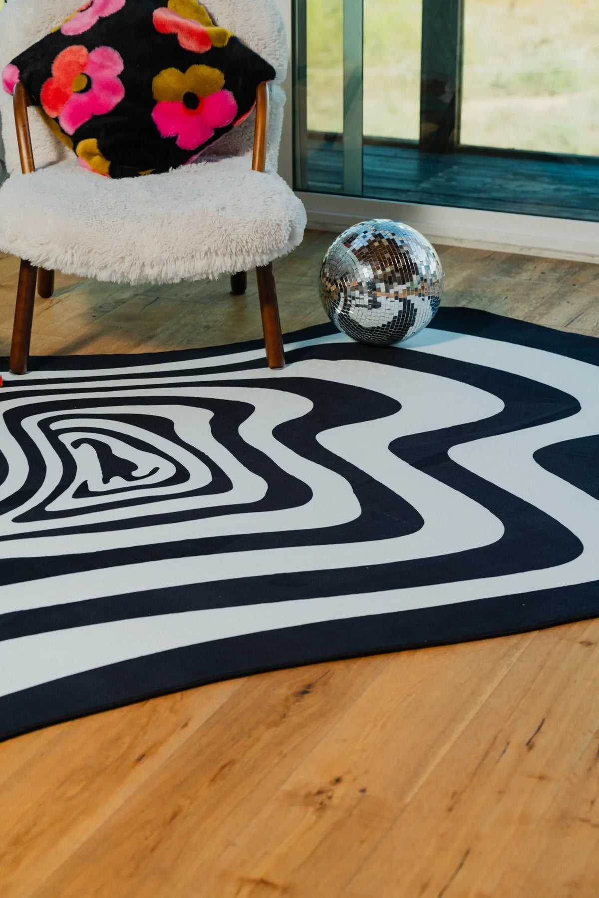 Curved edge of the rug with concentric black and white rings near a window and disco ball.
