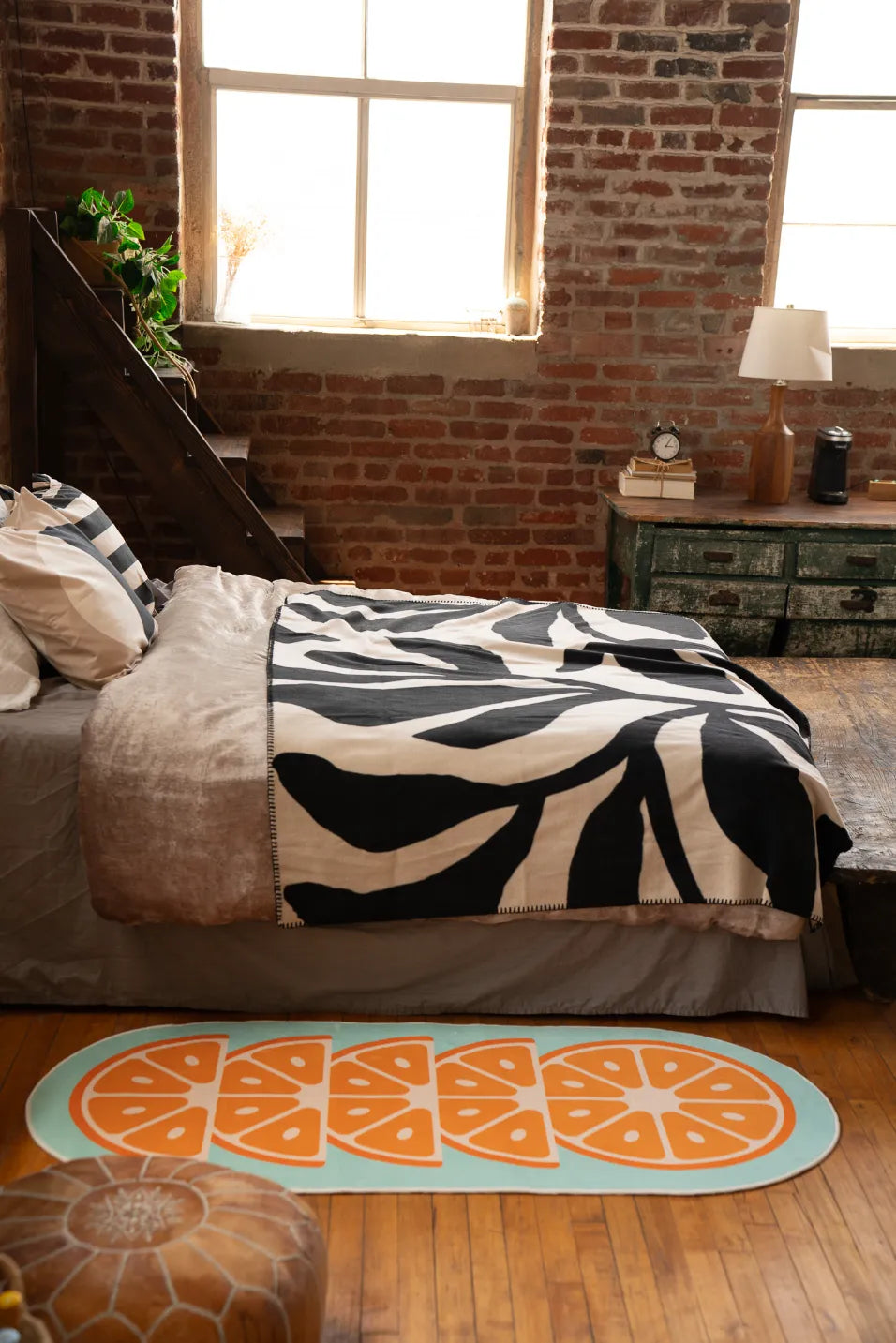 Blue rug with orange slice print on wood floor next to bed with zebra print sheet and leather pouf, home decor