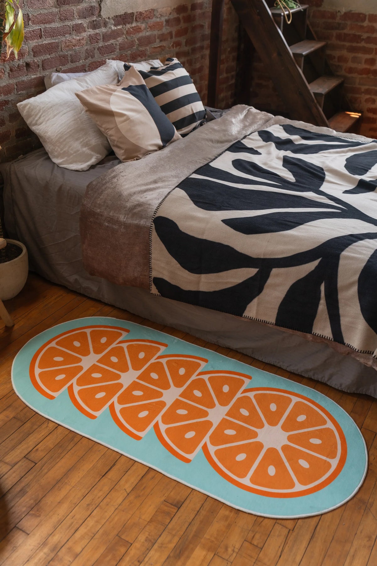 Oval orange slice rug on wooden floor beside bed with zebra-patterned bedding and beige throw, next to potted plant