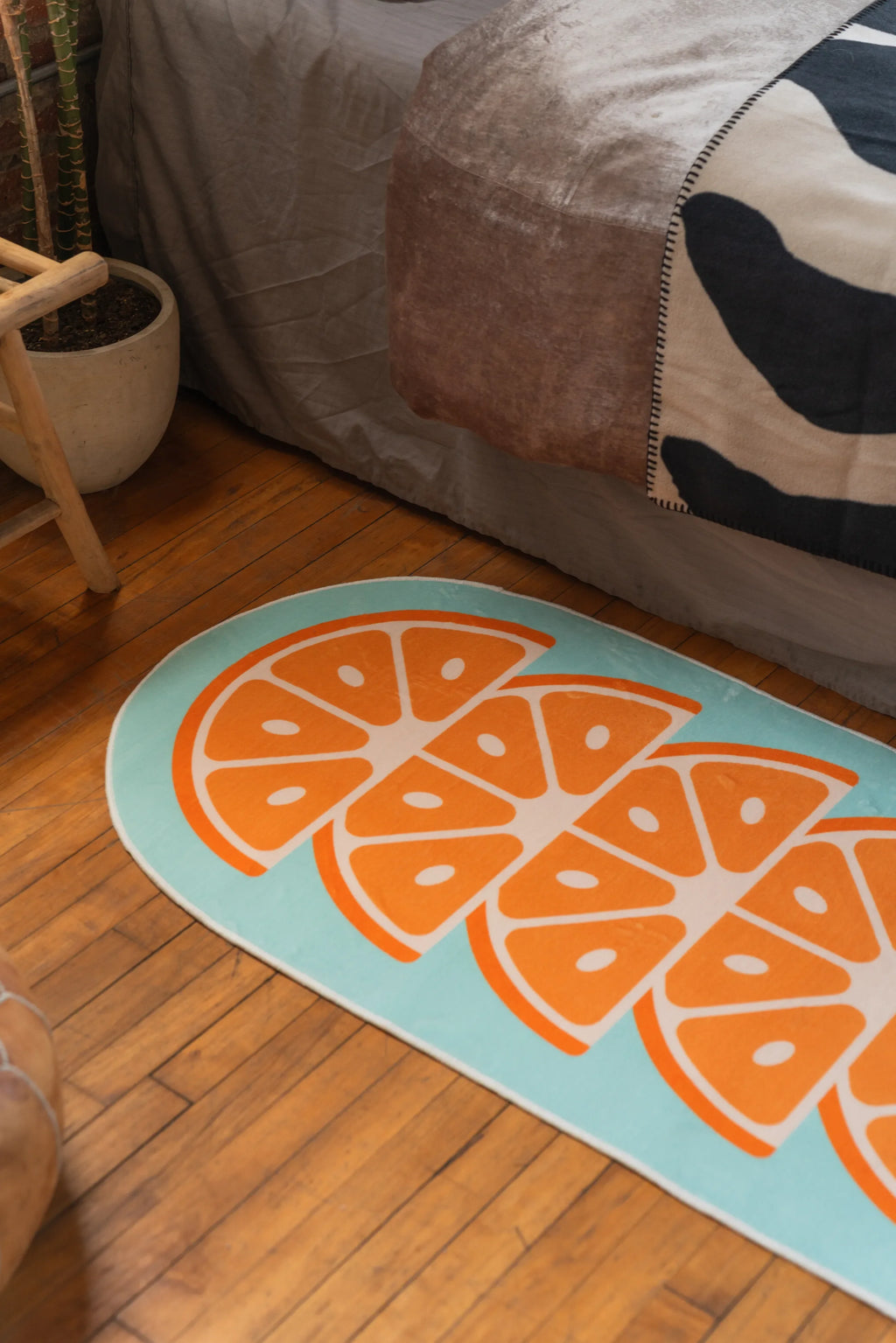 Close-up of oval citrus-themed rug with bright orange segments and blue border beside neutral bed setup