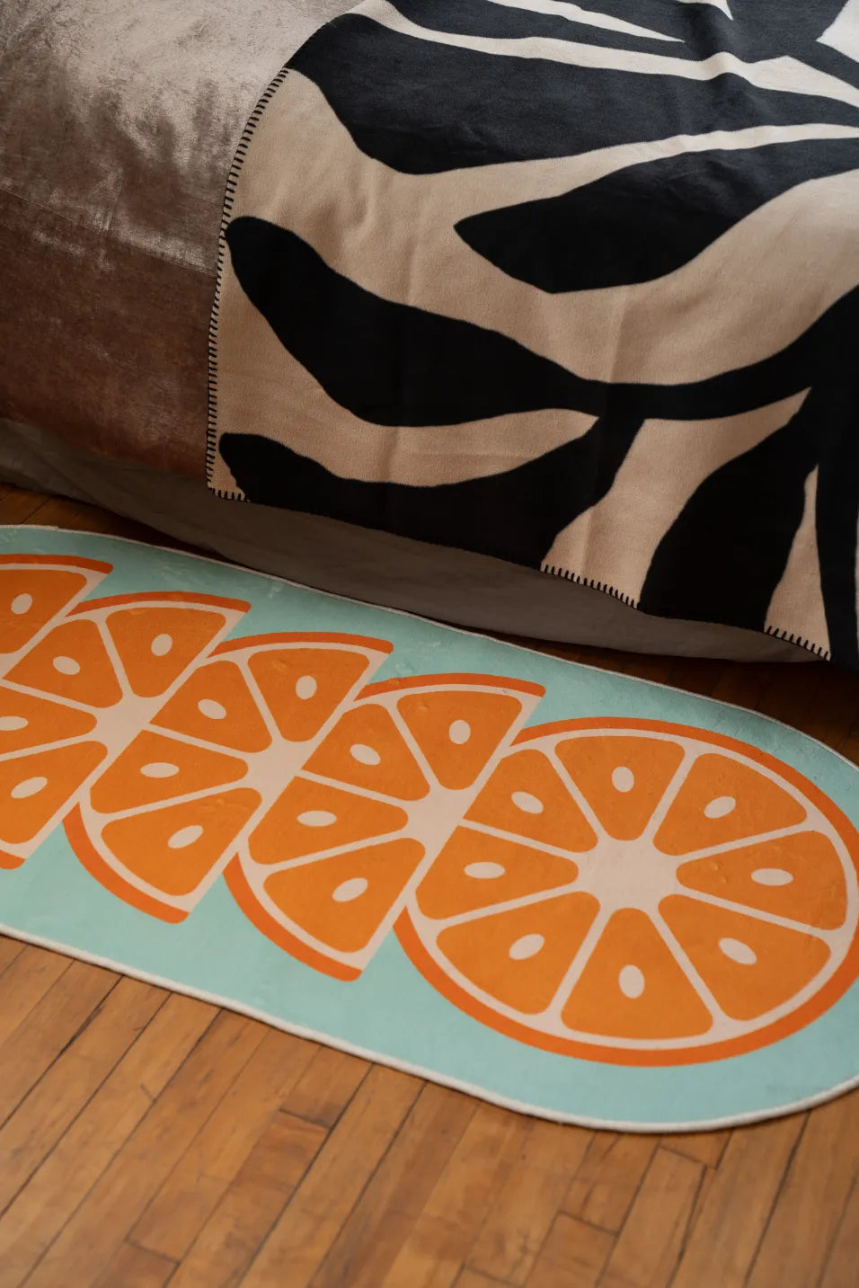 Orange slice patterned rug placed on floor near bed with black and white bedding, wood grain flooring visible