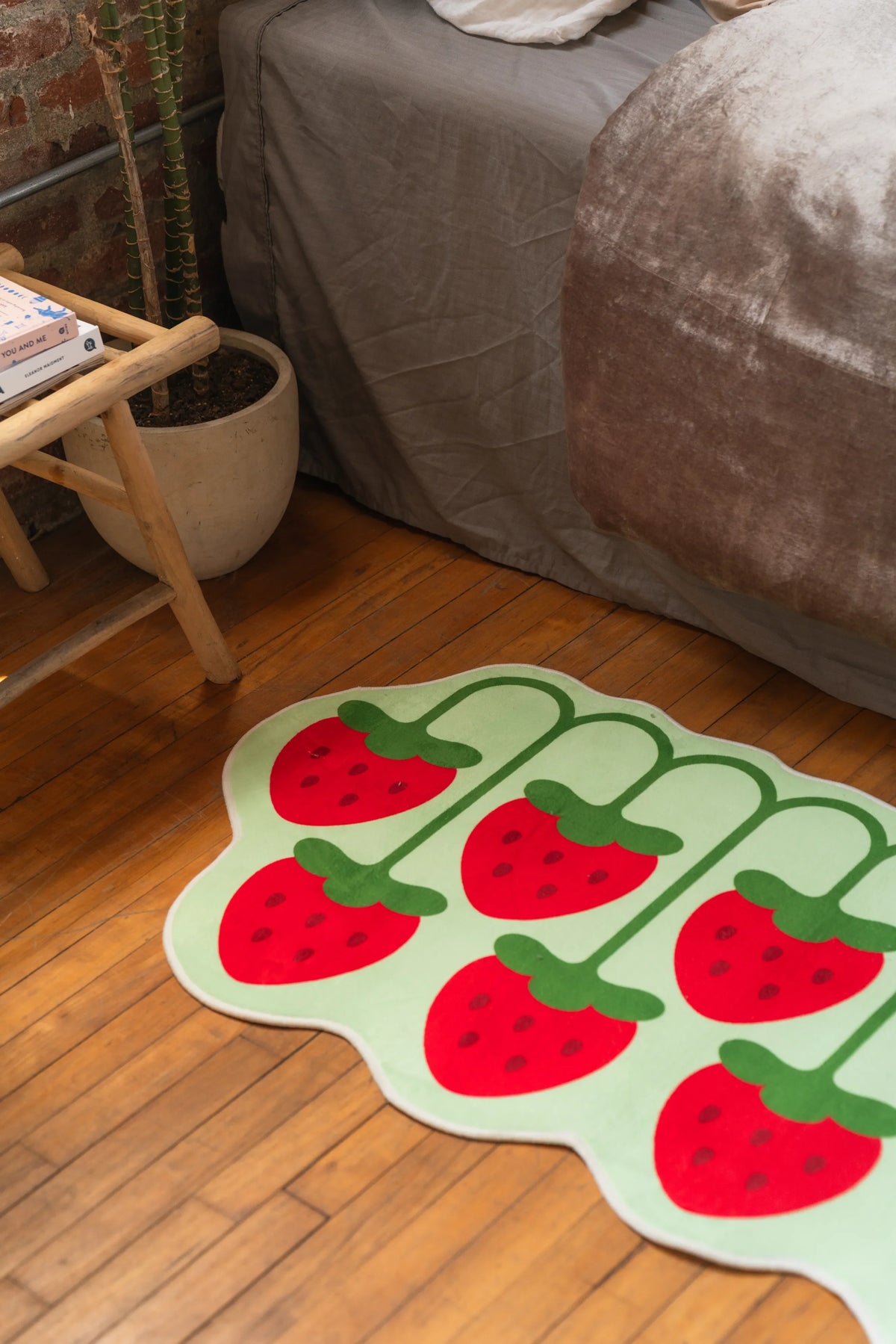 Playful strawberry design rug on hardwood floor near rustic wood table and gray bedding