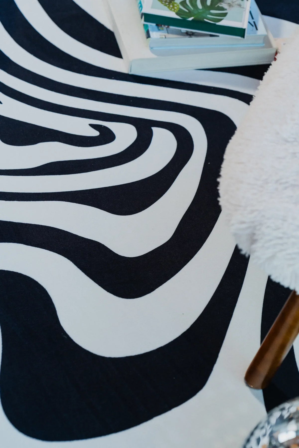 Close-up of abstract curves on the black and white rug, with books and a fuzzy chair leg adding texture to the cozy setting.