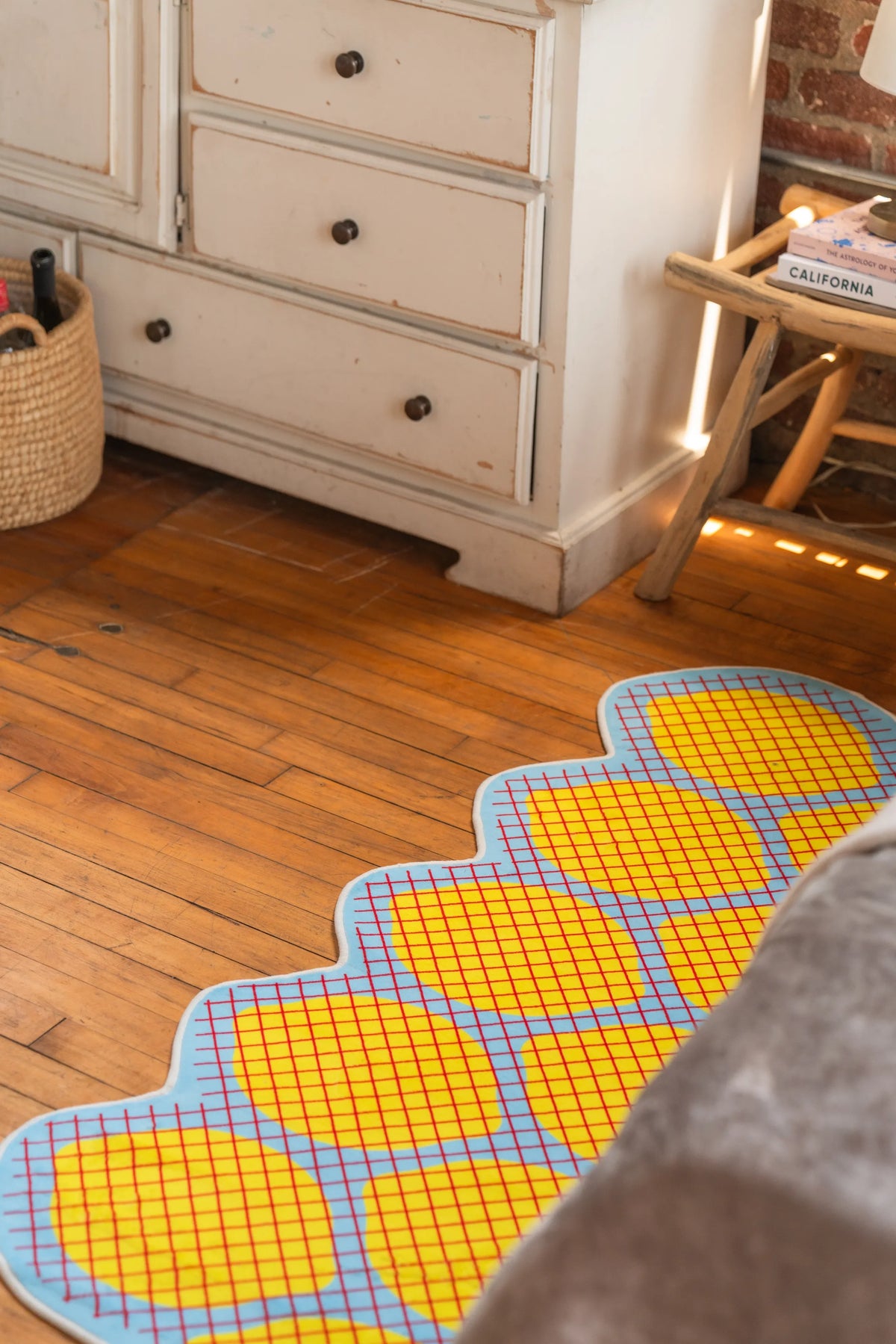 Playful yellow grid rug with blue trim on wooden floor near white dresser and woven basket