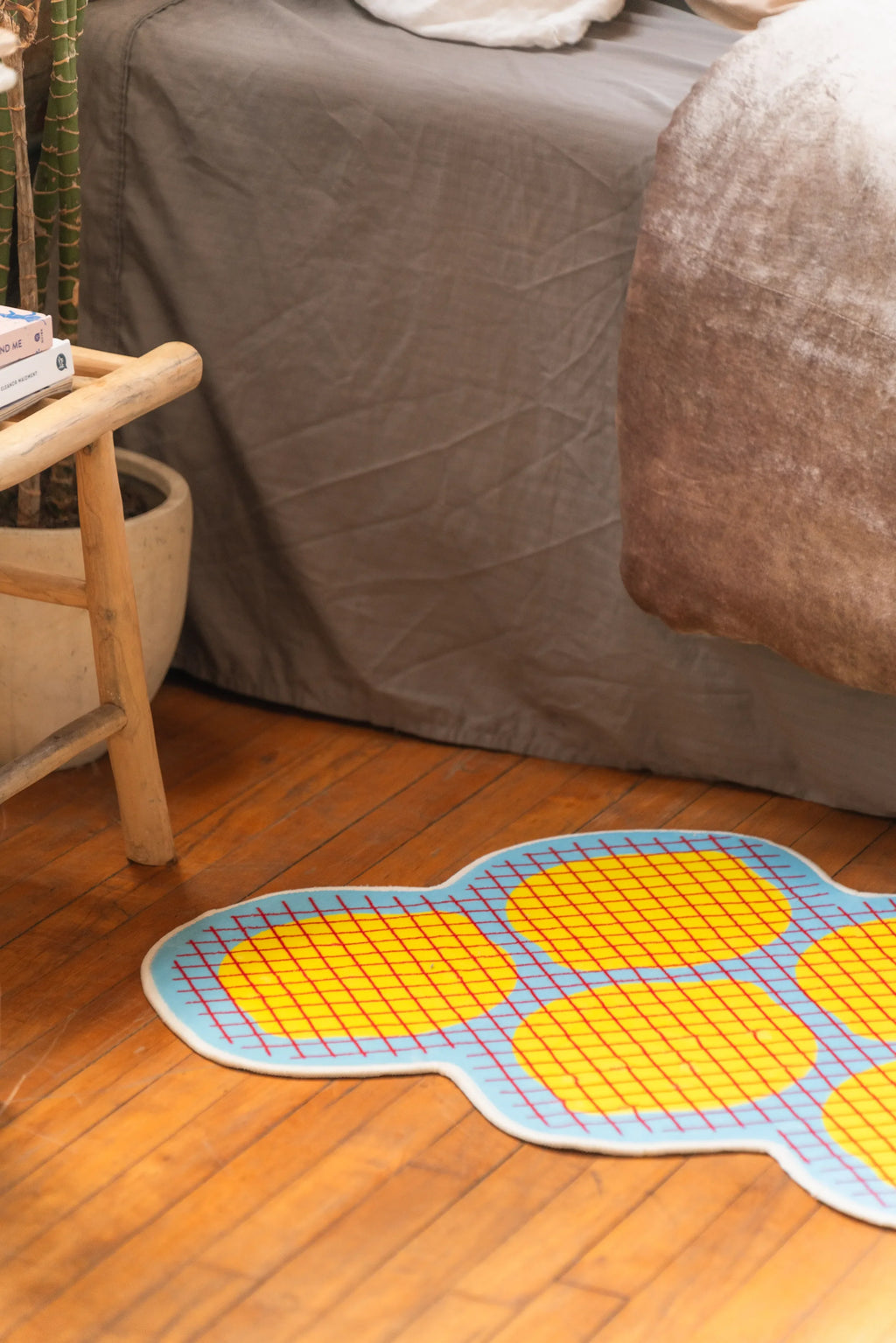 Irregular yellow grid bedroom rug beside bed and wooden stool on warm wood floor