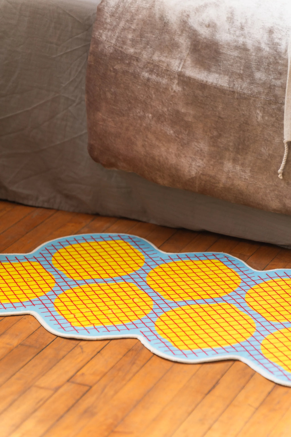 Wavy-edged yellow grid bedroom rug laid next to bed on hardwood floor