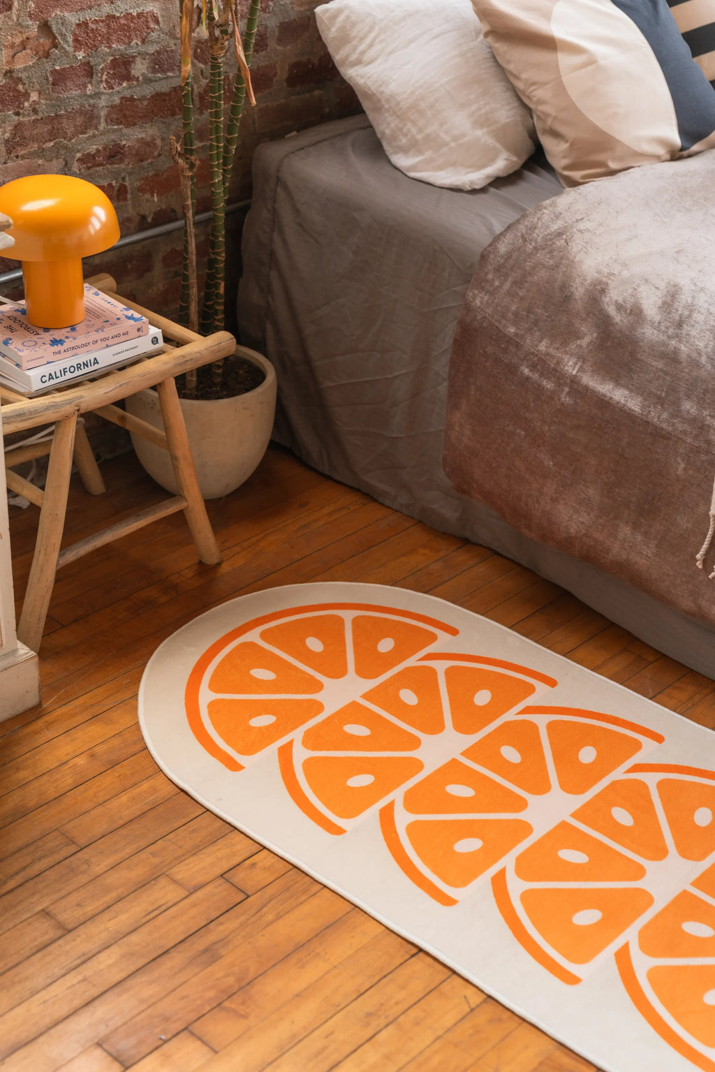 Close view of White Modern Orange Rug with juicy slice shapes, placed near bedside table holding books and orange mushroom lamp