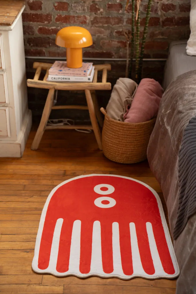 Orange abstract rug with rounded top, white eyes, and bold stripe legs, styled beside a basket and vintage side table