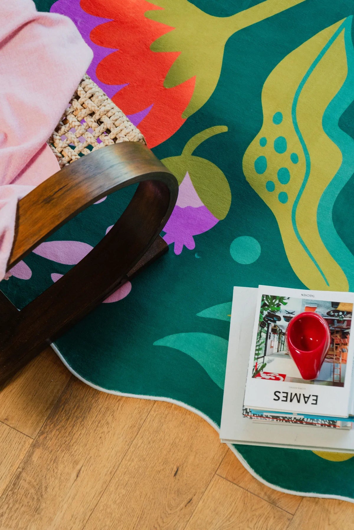 Detail of the floral wavy rug showing bold green and red motifs near a curved wood chair on floor.