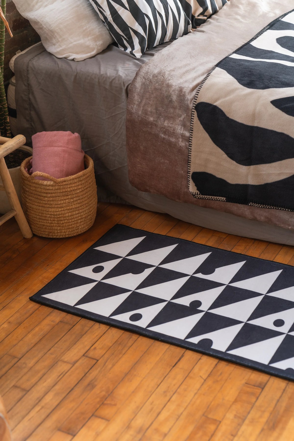 Modern monochrome triangle runner rug on wood floor next to bed styled with black and white textiles and a rattan basket