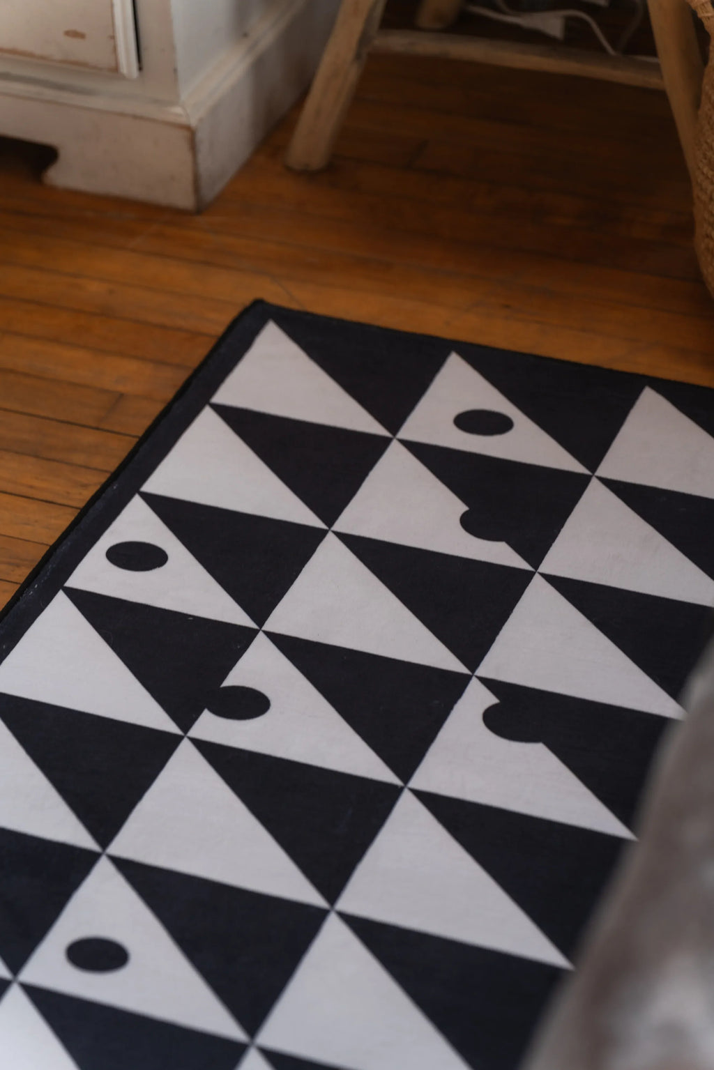 Close-up of minimalist geometric rug with alternating black and white triangles and abstract dot accents on clean woven texture