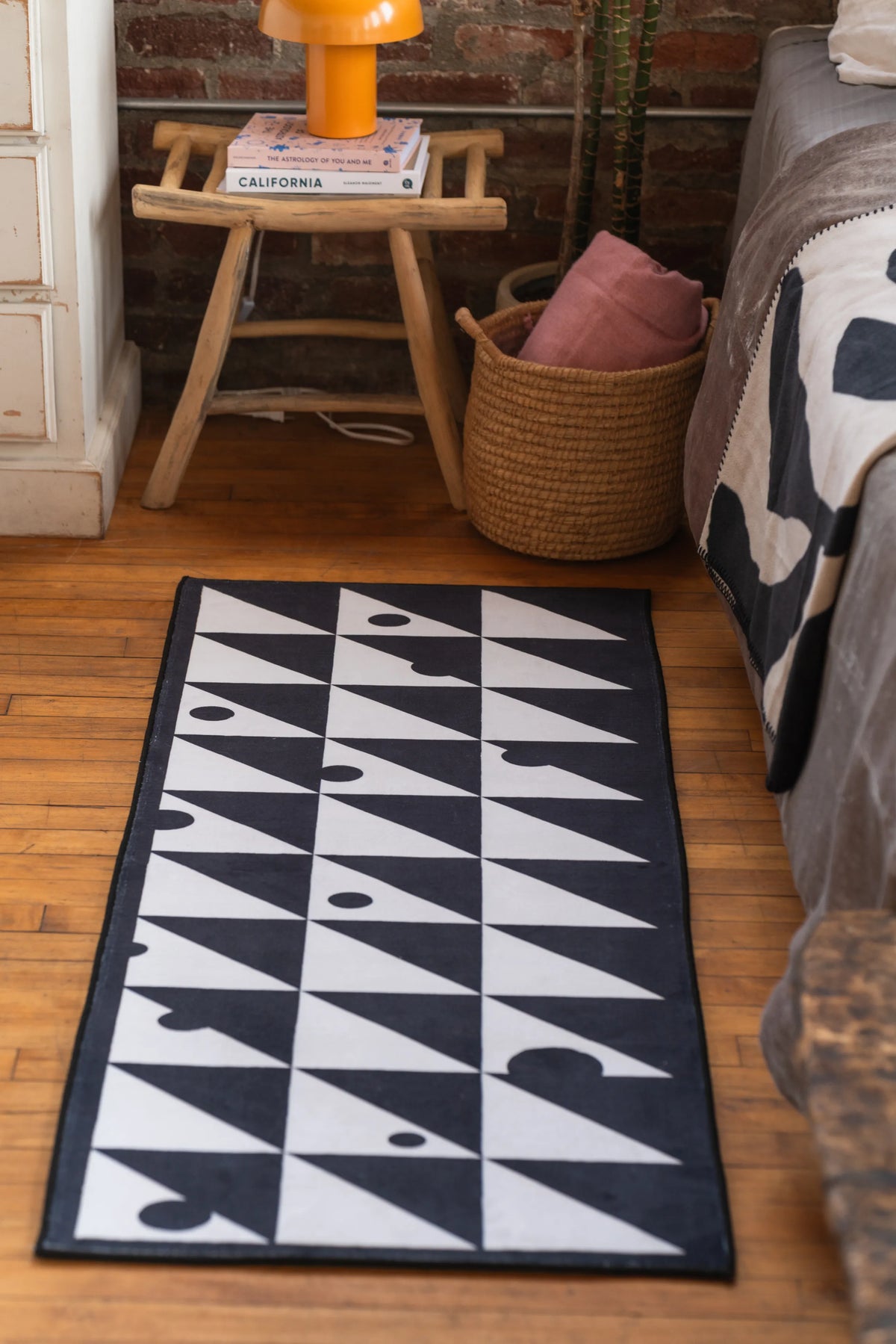 Black and white runner rug with geometric triangle pattern beside a bed with beige throw and round woven basket