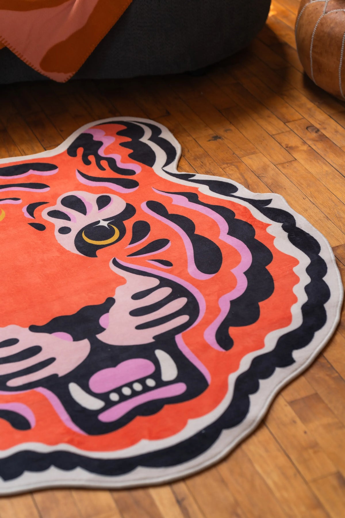 Close-up of a funky tiger rug with vibrant stripes, placed beside a dark sofa on natural wood floor.