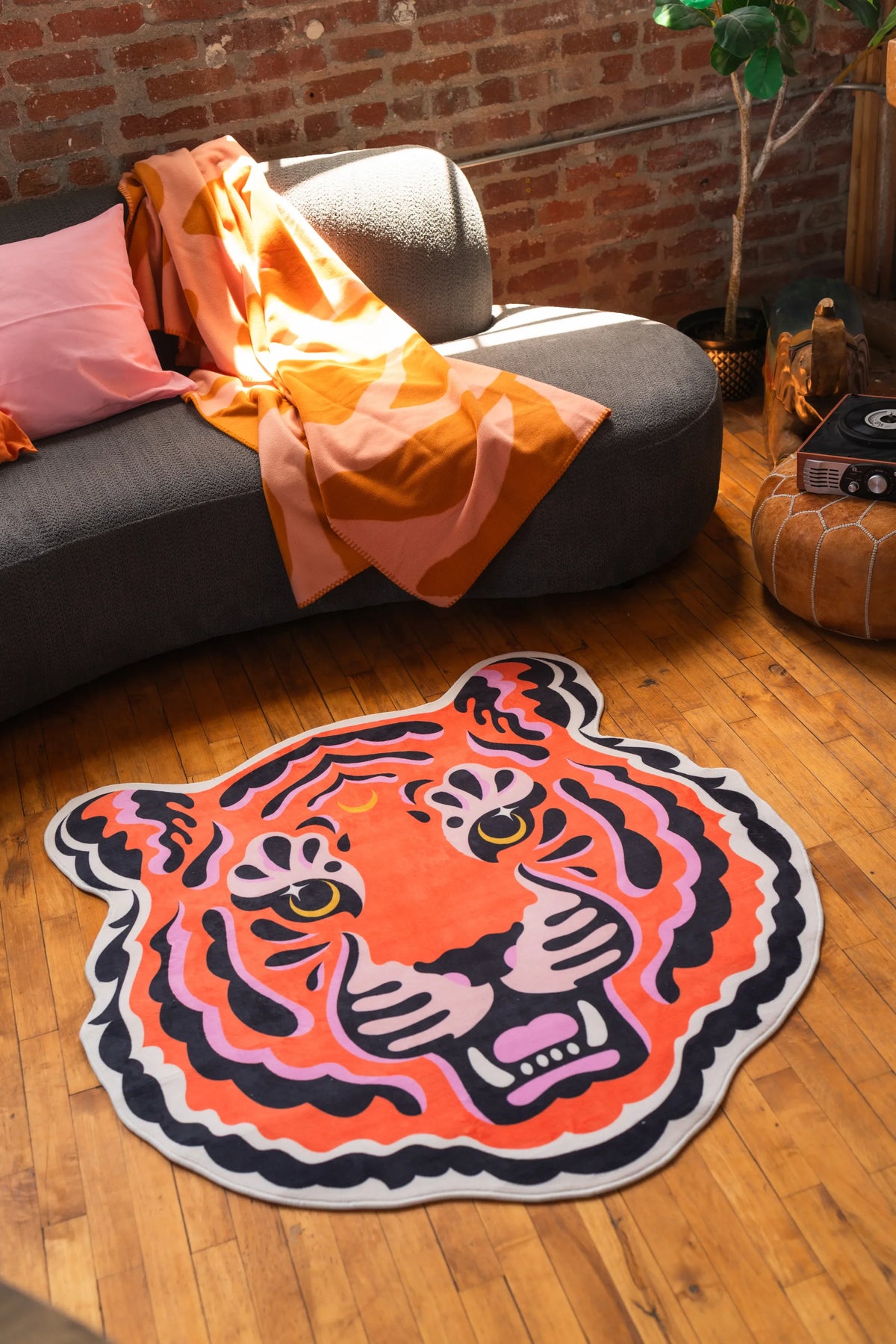 Funky statement tiger rug with vivid pink and orange tones by Jessica Miller, styled in a cozy corner with brick walls.