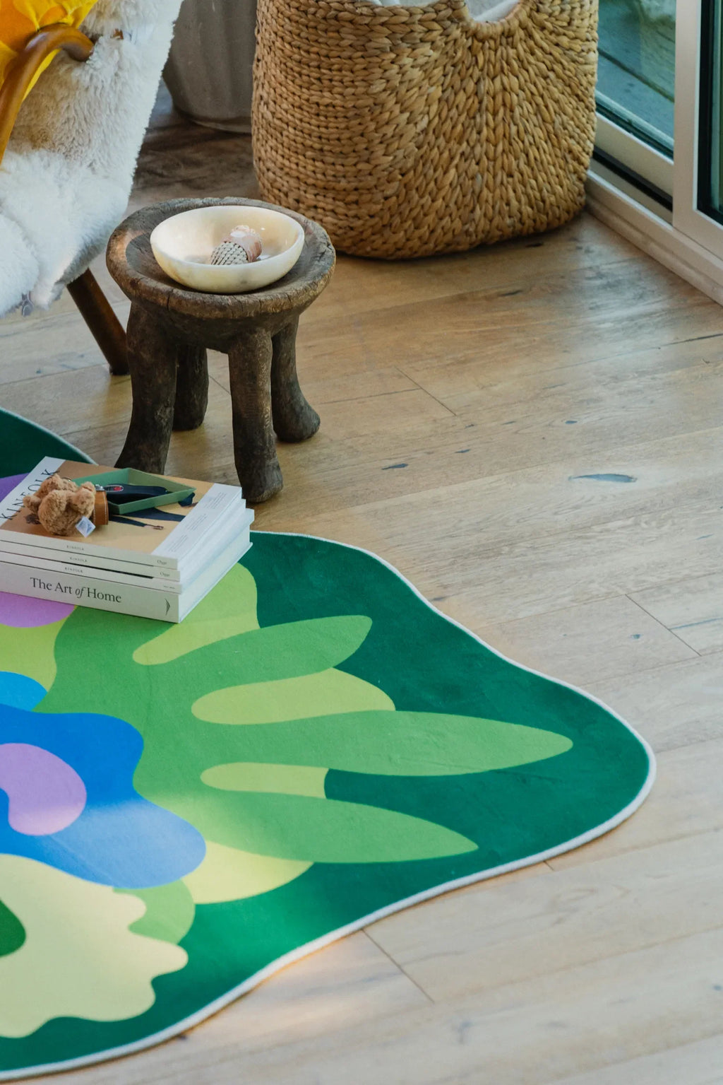Floral rug with green leaf edges beside a window nook in the living room, paired with wood floor and woven basket.