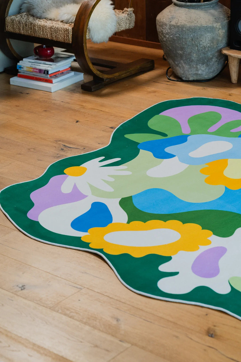Botanical floral rug with scalloped edges laid out beneath a chair and books in a cozy corner of the living room.