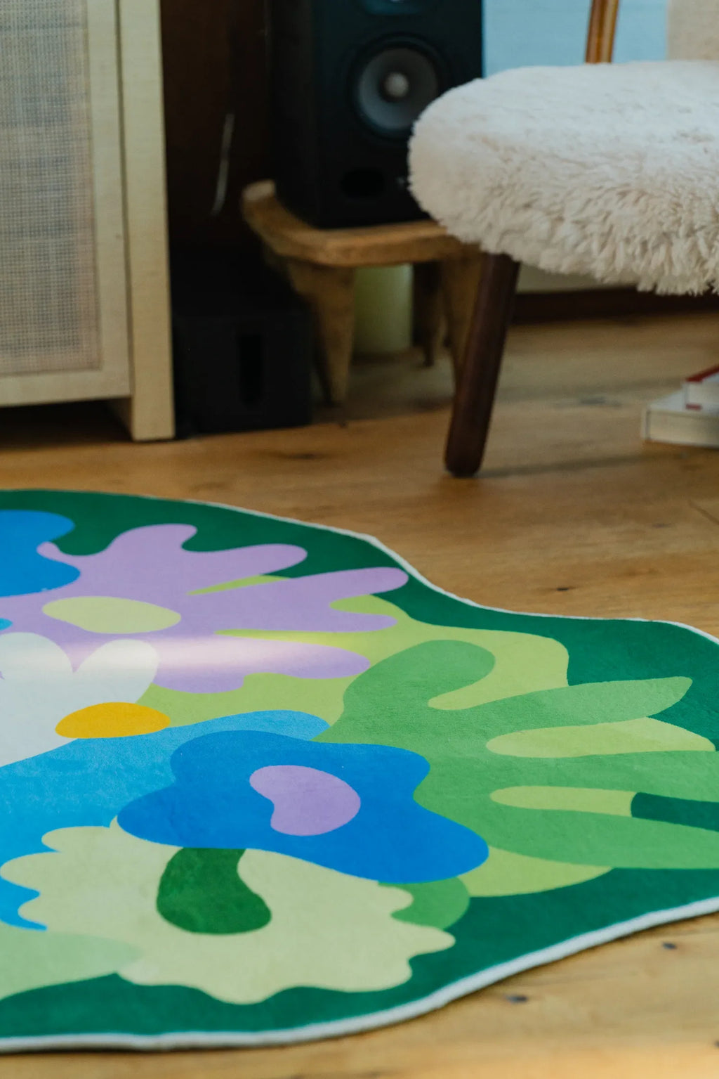 Corner of the botanical floral rug shown near a fuzzy stool and speaker cabinet in the living room.