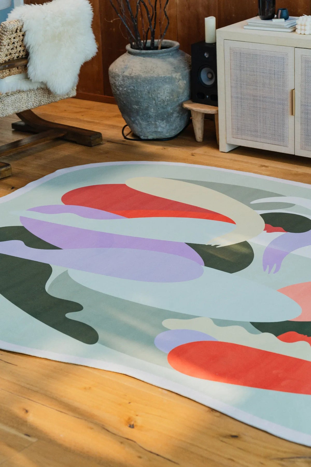 Detailed view of pastel rug featuring abstract human forms in soft greens, purples, and reds on wooden floorboards.