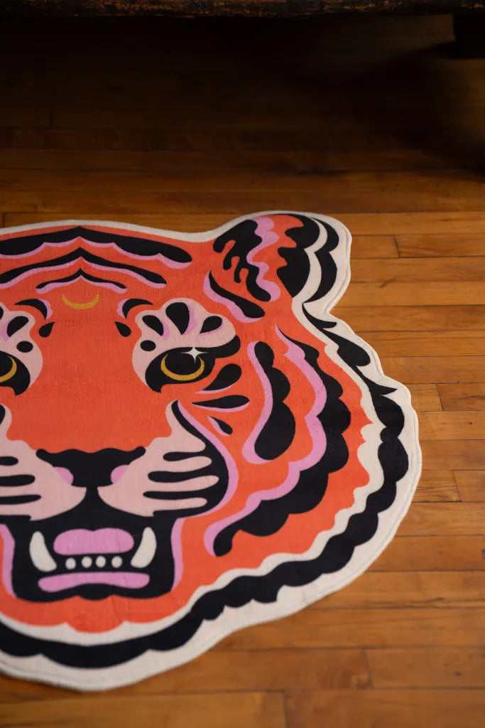 A cropped look at the funky tiger rug showing its bold colors and face detail, placed on wooden floorboards.