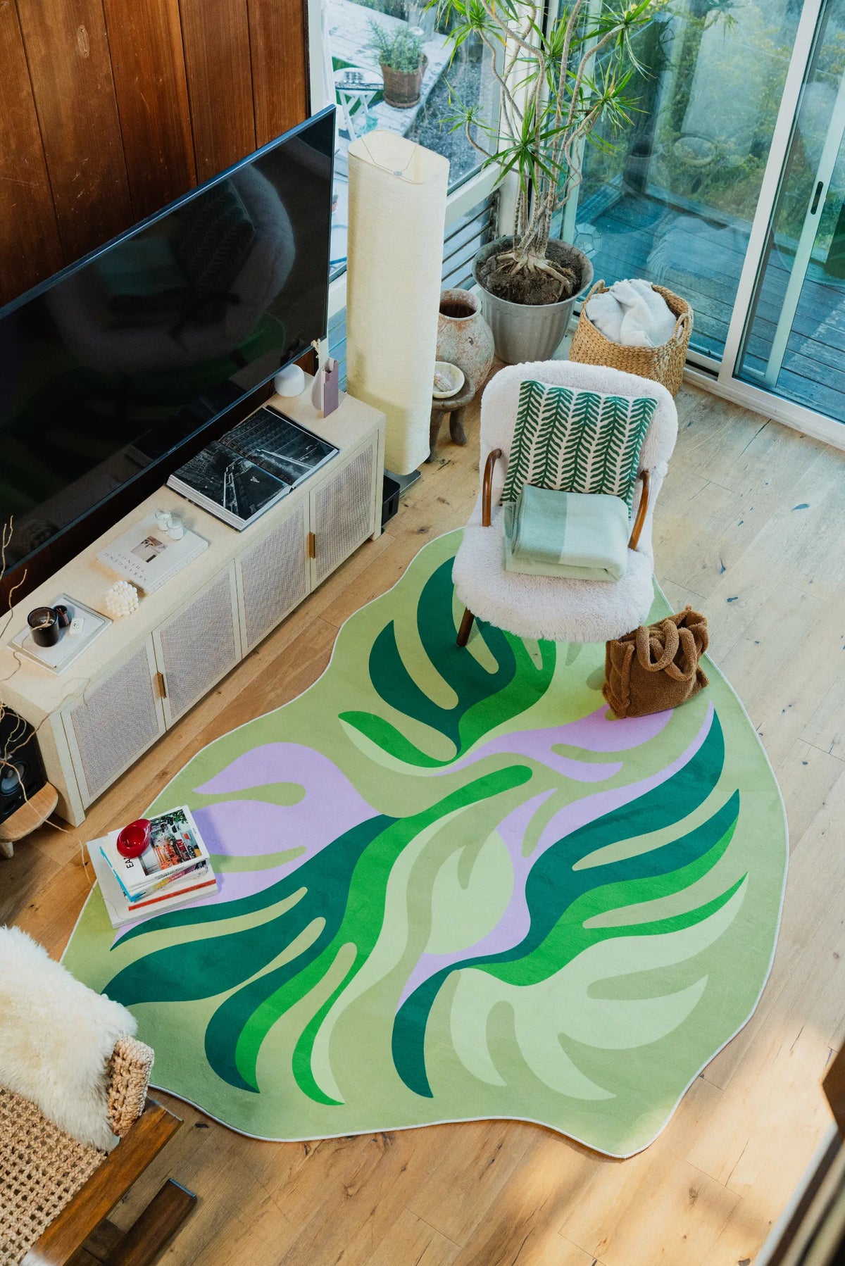 Botanical leaves rug paired with a boucle chair and green throw, styled near the TV console in a bright living room.