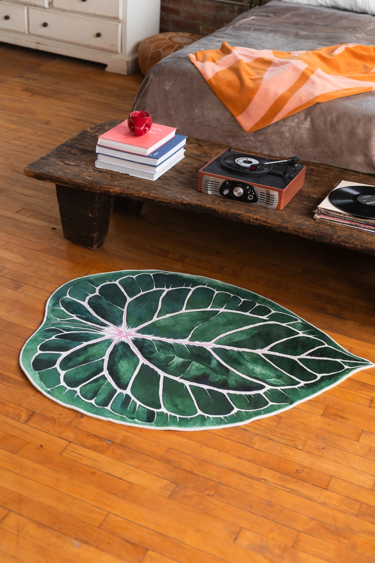 Leaf rug set near a low wooden table and bed, resting on warm wood floor in a softly lit vintage-style room.